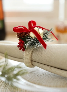 Detail of Christmas napkin ring with red bow, pine cone and bell on linen fabric