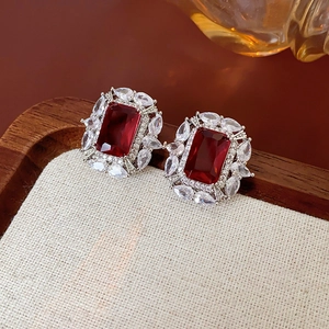 Détail de boucles d'oreilles zircon rouge avec halo de cristal blanc sur plateau en lin