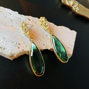 Close-up of teardrop emerald green glass earrings on a textured stone surface