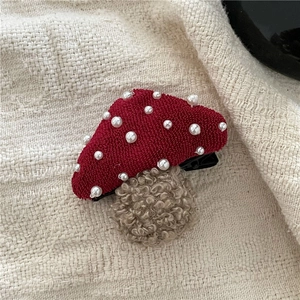 Detailed view of a red fabric mushroom hair clip with pearls on a beige woven surface