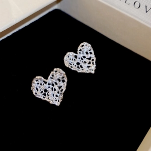 Macro shot of silver heart-shaped filigree earrings featuring intricate hollow lace texture