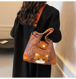 Detailed view of the brown quilted puffer tote bag featuring a 3D plush cat and orange strap