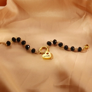 Dettaglio del ciondolo a cuore dorato con incisione LOVE e catena con perline nere