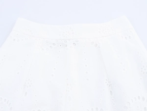 Detail of white cotton pants featuring intricate hollow-out floral embroidery on the waist