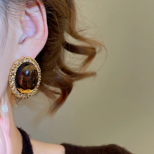 Close-up of gold oval resin earring with amber center and crystals on ear lobe