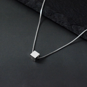 Minimalist silver cube pendant on box chain necklace over dark textured stone background