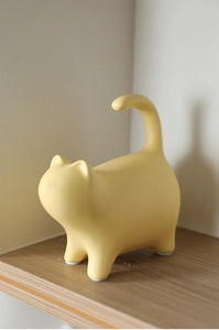 Close-up of a modern matte yellow ceramic cat ornament with smooth lines and long tail