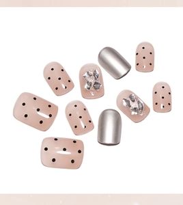 Detail of nude pink and silver press-on nails with black polka dots and diamond accents