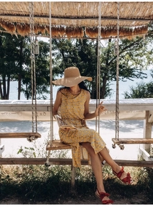 Gros plan sur une robe midi jaune fleurie sans manches avec chapeau de paille en bord de mer
