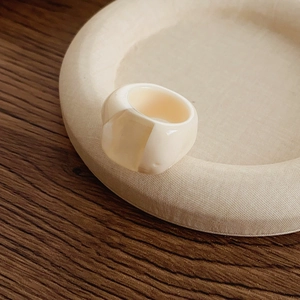 Minimalist cream resin ring detail resting on a woven texture tray with wood background