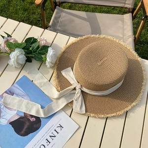 Detailed top view of straw sun hat with white bow and fringe edge on a table