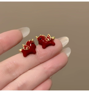 Macro shot of 18k gold plated red enamel mythical creature stud earrings on a fingertip
