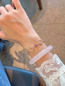Détail du bracelet trèfle en cristal et jonc en quartz rose sur un poignet en dentelle