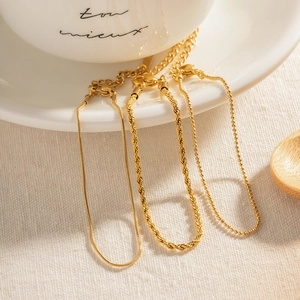 Detailed close-up of gold snake, rope, and bead chain jewelry on a white ceramic plate