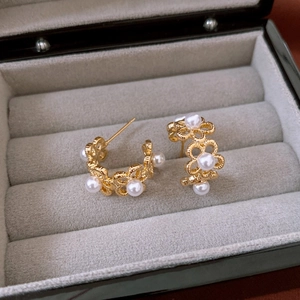 Detailed macro of gold plated hollow flower earrings with pearls on grey velvet