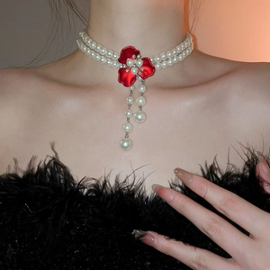 Detail of a double-layer pearl necklace featuring a red flower pendant and pearl tassels