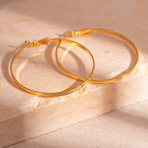 Detailed view of large gold geometric hoop earrings with textured finish on stone surface