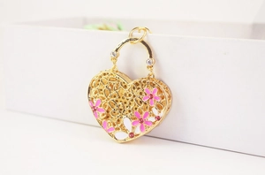 Detail of a golden hollow heart pendant with pink floral patterns and tiny gems