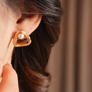 Detail of vintage tiger eye and pearl earrings on model with gold triangle frame