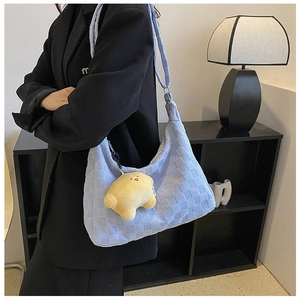 Detail of light blue checkered plush tote bag with yellow smiley face charm on a model