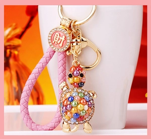 Detail of turtle keychain with rhinestone shell, pink woven strap and lucky charm