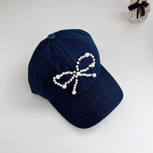 Close-up of pearl bow decoration on dark blue washed denim baseball cap for women