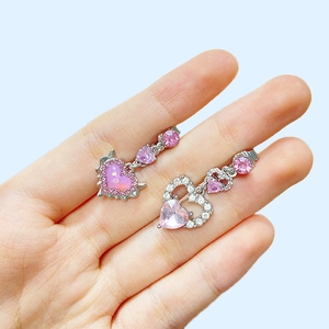 Close-up of asymmetric silver heart earrings with pink gemstones on a palm