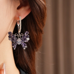 Detail of silver butterfly hoop earrings with purple and clear zirconias worn by a model