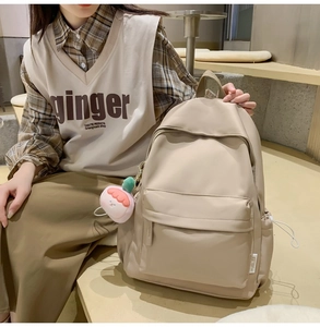 Close-up of beige nylon backpack with peach plush pendant worn by a female model