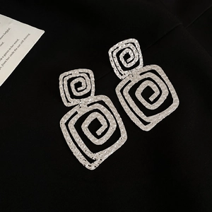 Macro view of textured silver double square spiral earrings on a black fabric backdrop