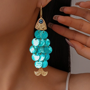 Close-up of fish-shaped turquoise shell earrings with golden evil eye detail on model