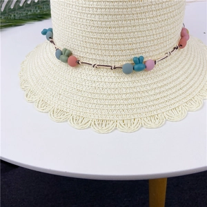 Detail of straw hat with colorful beads, rabbit charms and a wavy scalloped brim