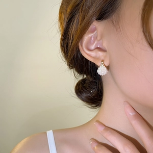 Detail of small fan-shaped pearl drop earrings on model with golden metal hooks
