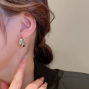 Gros plan d'une boucle d'oreille en C torsadée argentée au fini métal poli