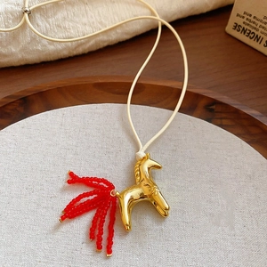Gold-plated pony necklace with red bead tassel and beige cord on a wooden tray
