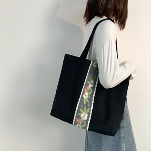 Dettaglio del ricamo floreale su borsa tote in tela nera indossata a spalla da una modella