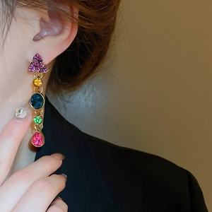 Close-up of long gold earrings with colorful gemstone drops on a female model