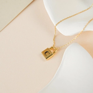 Detail shot of a golden lock pendant necklace with black engraved letter C on a white surface
