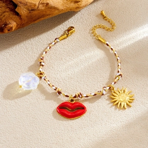 Bohemian braided cord bracelet with red lips and gold sun charms on sandy texture