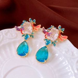 Macro shot of gold plated earrings featuring colorful enamel butterflies and blue gemstones