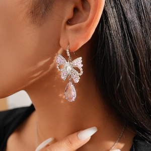 Close-up of bow earrings with pink teardrop crystal pendant worn by a model