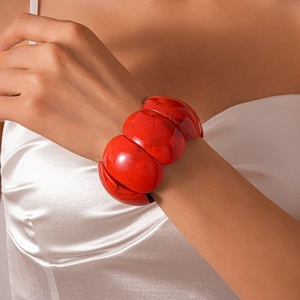 Close-up of a wide red marbled acrylic chunky bracelet worn on a white silk sleeve