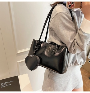 Detail of a black shiny leather tote bag featuring a matching heart-shaped coin purse charm