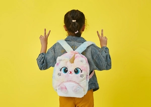 Detail of a plush rainbow tie-dye unicorn backpack on a child wearing a denim jacket