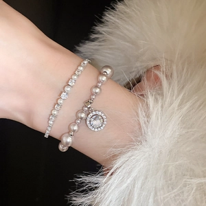 Detail of layered silver zircon tennis bracelet with elegant pearls on a soft fur background