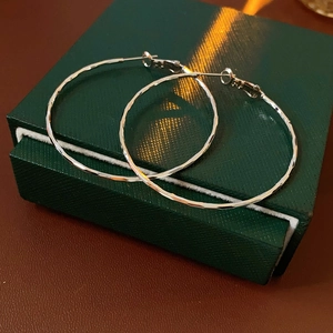 Détail macro de créoles argentées avec texture martelée sur une boîte à bijoux de luxe