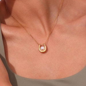 Detail of 18K gold U-shaped horseshoe pendant necklace with a round lustrous pearl