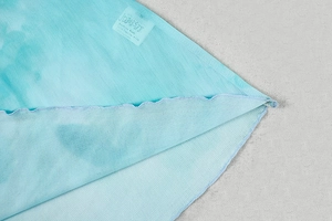 Detail of light blue tie-dye fabric with ribbed texture and wavy hem design with size label