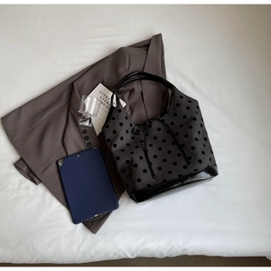 Flat lay of gray polka dot canvas tote bag with black leather bottom and office essentials