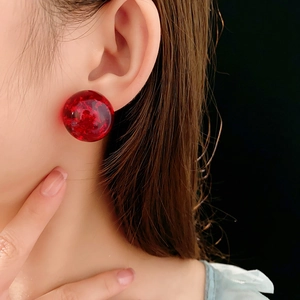 Macro view of red resin stud earrings with gold foil texture on female model's ear